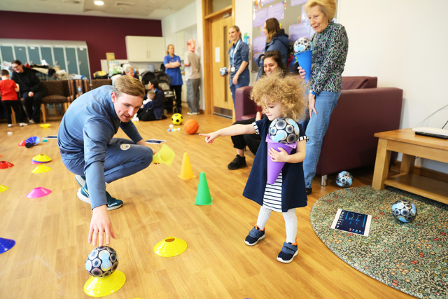 A child holding blue cones with balls interacts with an adult in a room set up with colorful cones for a playful activity.