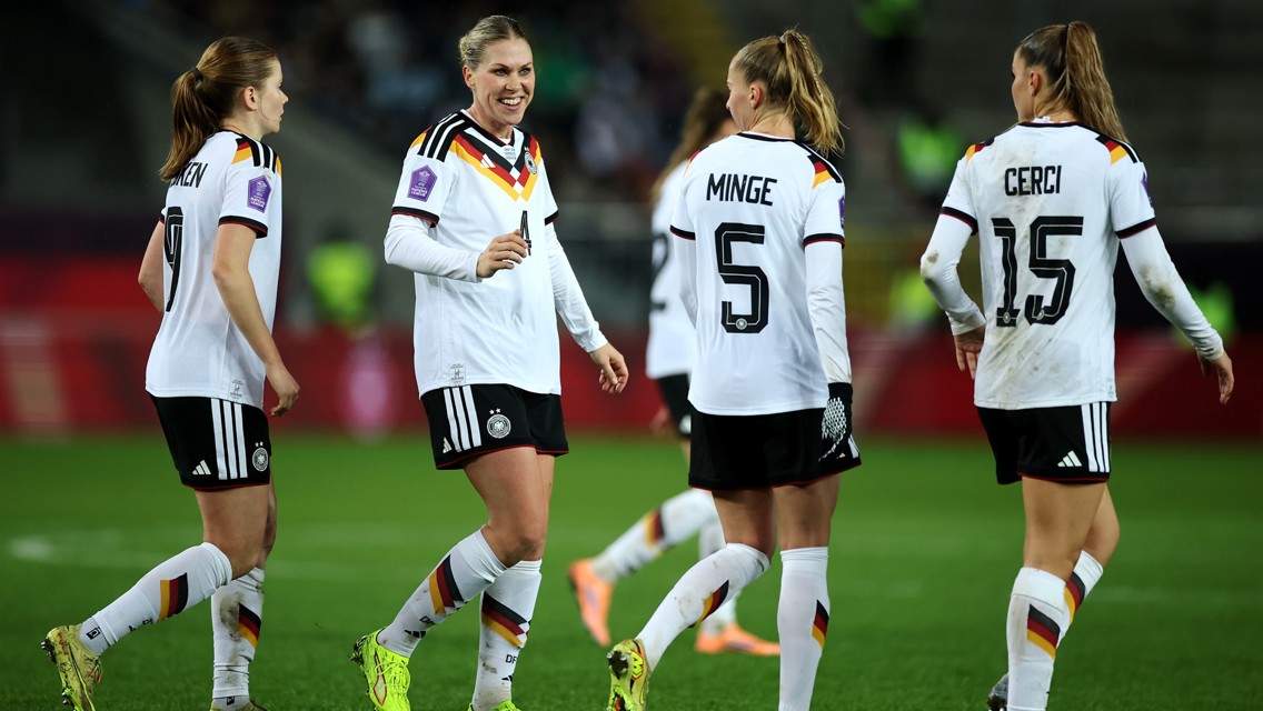 The image shows four female German soccer players on the field, wearing white jerseys with black shorts and socks. The visible names on their jerseys are 'CERCI,' 'MINGE,' and player numbers are seen including 5 and 15.