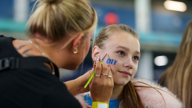 A person is piercing the ear of another individual in a casual setting. Both are indoors with attention focused on the ear.