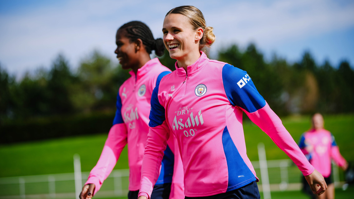 Two Manchester City women's team players in pink training gear on a field.