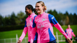 Two Manchester City women's team players in pink training gear on a field.
