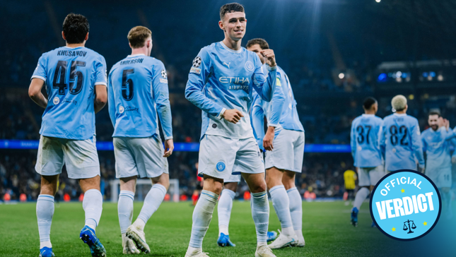 Players in Manchester City jerseys celebrating a goal on a soccer field during a match with a stadium crowd in the background.