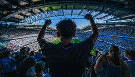 A football fan cheering with arms raised in a full stadium.