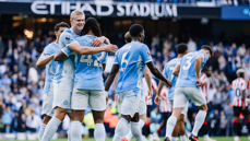 Manchester City players celebrate a goal at Etihad Stadium during a match, wearing light blue jerseys with white accents.