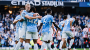 Manchester City players celebrate a goal at Etihad Stadium during a match, wearing light blue jerseys with white accents.