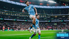 Manchester City players celebrating on the field after winning the Carabao Cup 2026. The background shows a cheering crowd inside a stadium.