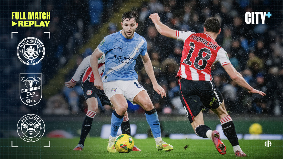 Manchester City player in blue kit competing against Brentford player during Carabao Cup match with logos of Manchester City, Carabao Cup, and Brentford FC displayed.