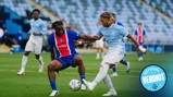 Two players compete for the ball during a soccer match between teams with PSG and Manchester City kits, with the background showing blurred stadium seats.