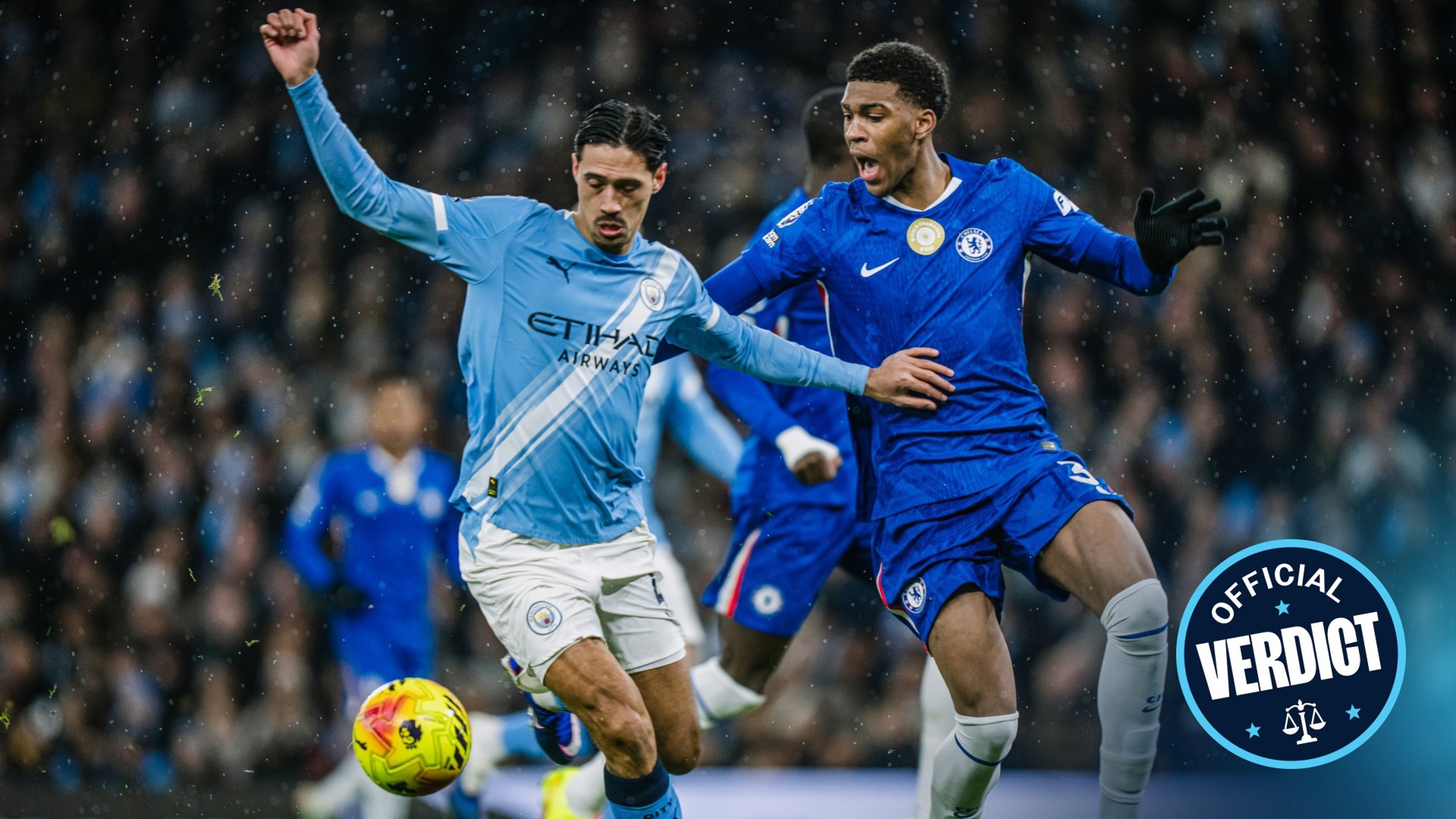 Two soccer players in action during a match, one wearing a Manchester City uniform and the other wearing a Chelsea uniform. Both are competing for control of the ball.