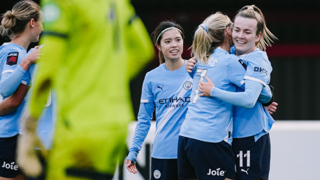 Manchester City Women's football players celebrating during a match. The players are wearing light blue kits, featuring the Manchester City crest and sponsor logos.