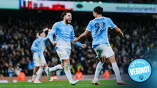 Manchester City players in a light blue kit celebrating a goal on the field during a match, with an 'Official Verdict' badge in the corner.
