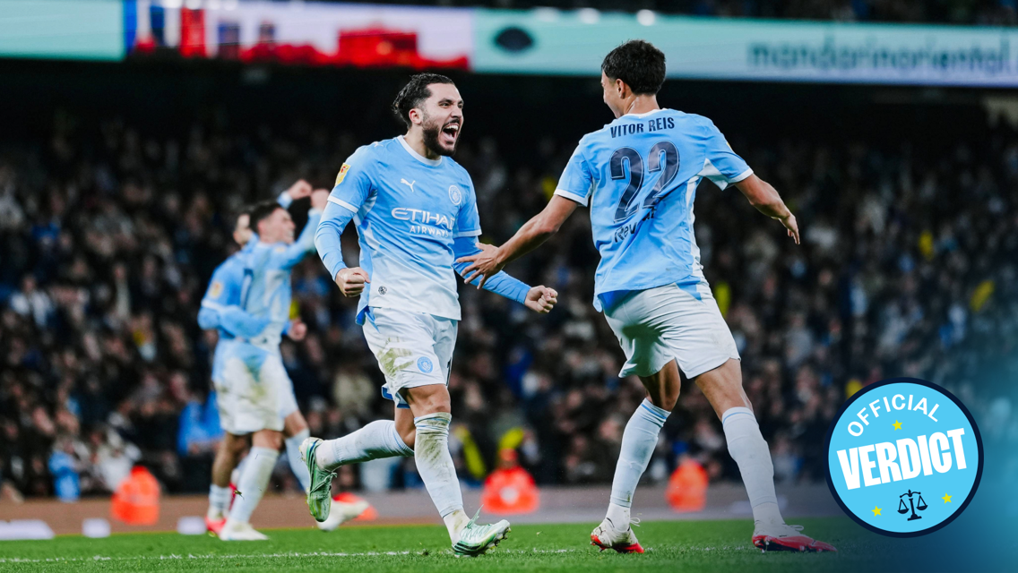 Manchester City players in a light blue kit celebrating a goal on the field during a match, with an 'Official Verdict' badge in the corner.