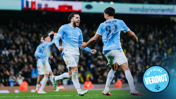 Manchester City players in a light blue kit celebrating a goal on the field during a match, with an 'Official Verdict' badge in the corner.
