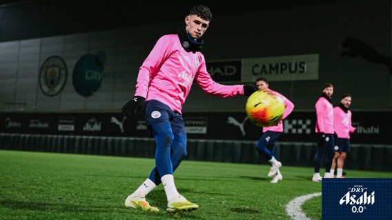 Football players in pink jerseys practicing on a field at Manchester City campus. A player is controlling a ball.