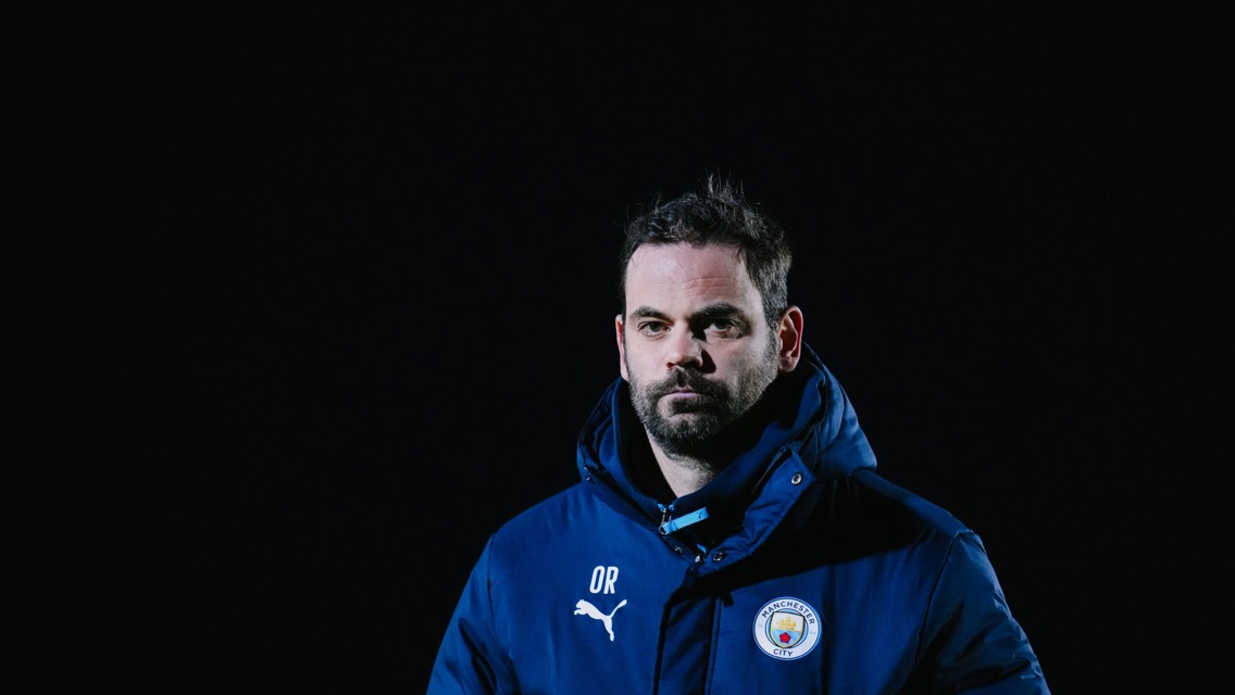 A person wearing a Manchester City jacket with Puma branding and the club crest, labeled with initials 'OR'.