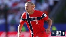 A football player wearing a red Norway jersey with the number 9 during a match, featuring Manchester City's branding and World Cup elements.