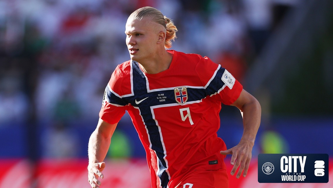 A football player wearing a red Norway jersey with the number 9 during a match, featuring Manchester City's branding and World Cup elements.