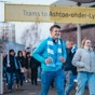 Group of people walking under a yellow sign that reads 'Trams to Ashton-under-Lyne'.