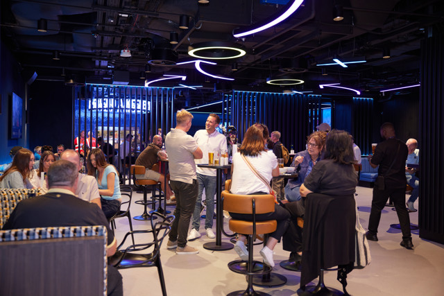 People socializing in a modern bar with neon lights and circular ceiling designs.