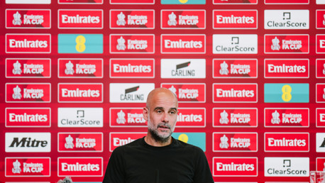 A person sits at a press conference table with a background of Emirates FA Cup logos and sponsors’ banners.