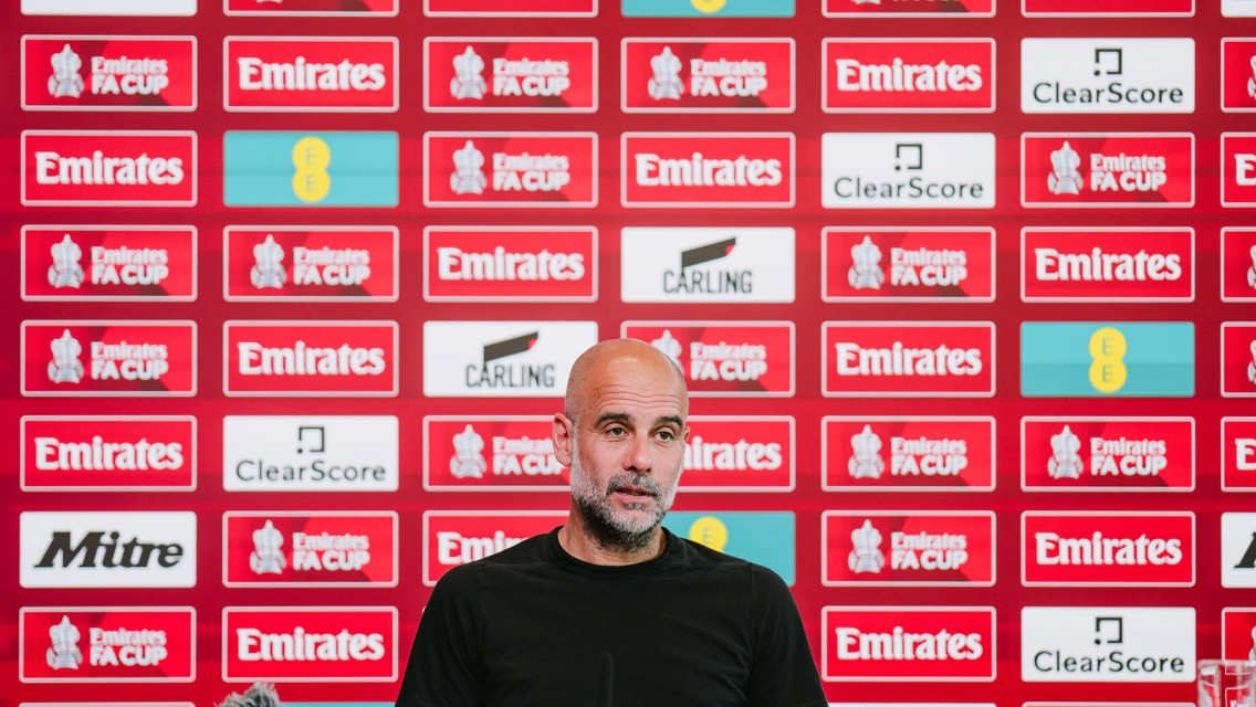 A person sits at a press conference table with a background of Emirates FA Cup logos and sponsors’ banners.
