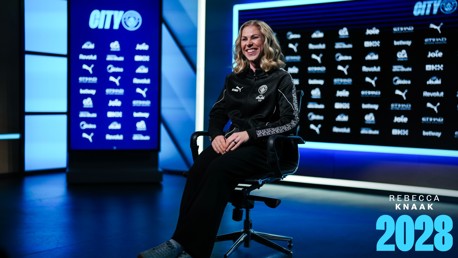 Rebecca Knaak seated for photo in a Manchester City setting, showcasing her contract extension to 2028.