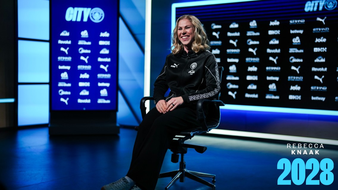 Rebecca Knaak seated for photo in a Manchester City setting, showcasing her contract extension to 2028.