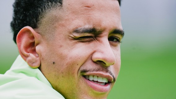 Image displaying the left ear and part of the neck of a person with curly hair, with the face and remaining details blurred. The image background is out of focus, showing green and gray tones.