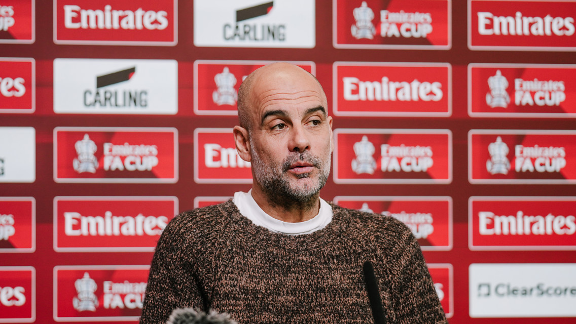 Person at a press conference with Emirates FA Cup branding in the background.