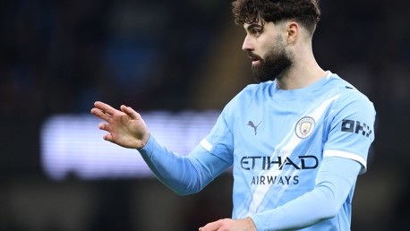 A Manchester City football player with a blurred face, wearing the team’s light blue jersey on the field.