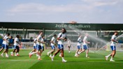 Soccer players training at Joie Stadium with sprinklers in the background. They are wearing white and blue uniforms.