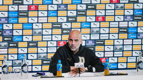 A person at a press conference table wearing a black jacket with the letter 'P' logo. Background shows a wall with logos including Puma and Etihad.