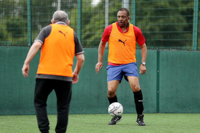 Two football players wearing orange training bibs during a training session, one dribbling the ball while the other defends.