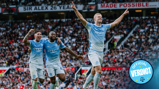 Three Manchester City players in blue uniforms celebrate a goal at Old Trafford. They raise their arms in triumph as the crowd looks on. A logo that reads 'Official Verdict' is visible.