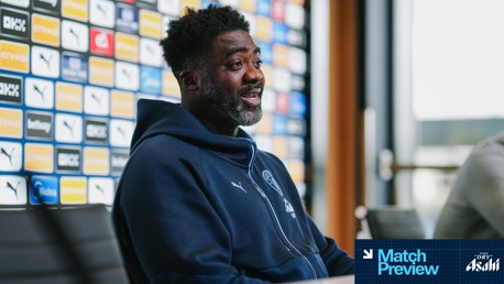 A person wearing a Manchester City hoodie at a press conference. Sponsor logos are visible in the background.