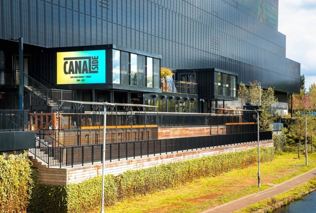 Modern building exterior featuring a sign for 'Canal Side' with surrounding greenery and a canal path.