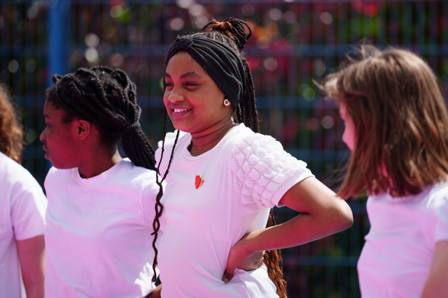Children wearing white shirts participate in an outdoor activity. Their faces are blurred to ensure privacy.