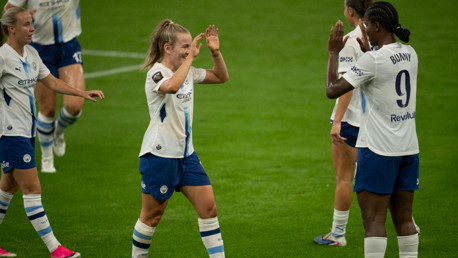 Manchester City women's soccer players celebrating with a high five on the field. One player has 'Bunny' and number 9 on her back.
