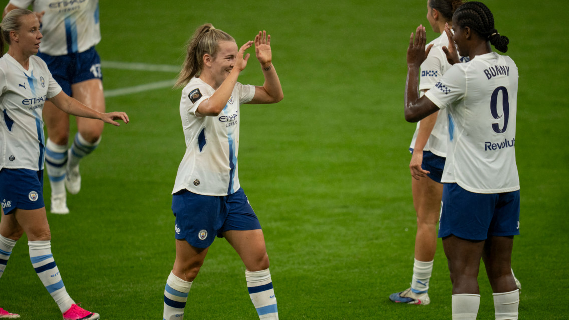 Manchester City women's soccer players celebrating with a high five on the field. One player has 'Bunny' and number 9 on her back.
