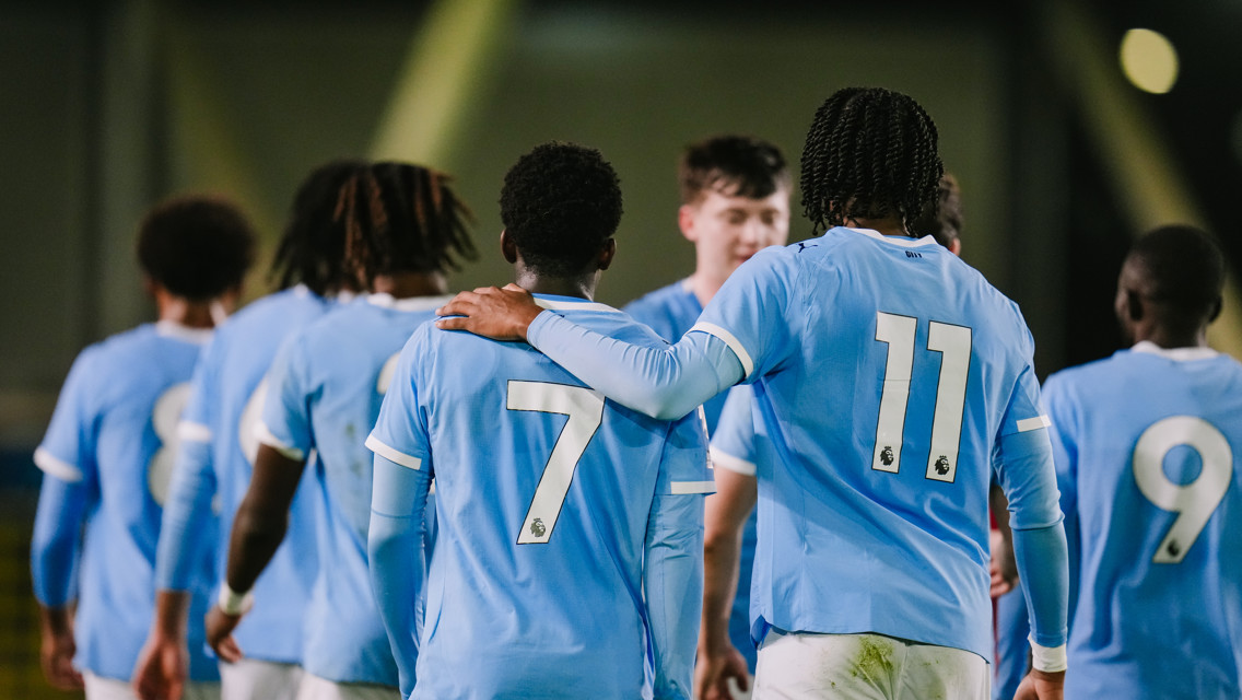 A group of young football players in light blue jerseys with numbers 7 and 11 visible, standing together on a soccer field.