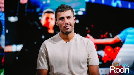 A man wearing a light beige shirt sits in front of a colorful backdrop. The words 'Thank you Rodri' are displayed on the image.