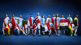 Group of 16 people wearing Manchester City kits, each with a different national flag draped over their shoulders, standing against a blue background.