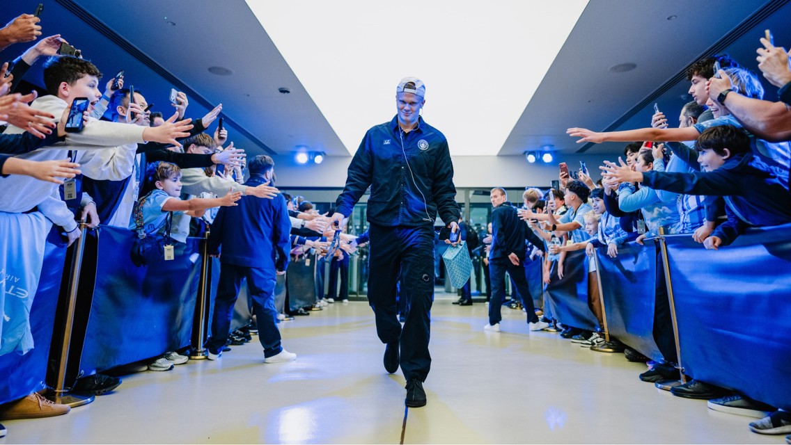 A football player is walking through a corridor, high-fiving fans lined up on both sides. The atmosphere is celebratory with people reaching out and taking photos.