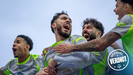 A group of soccer players huddling together, wearing gray and neon green jerseys. The image includes a sticker that says 'Official Verdict.'