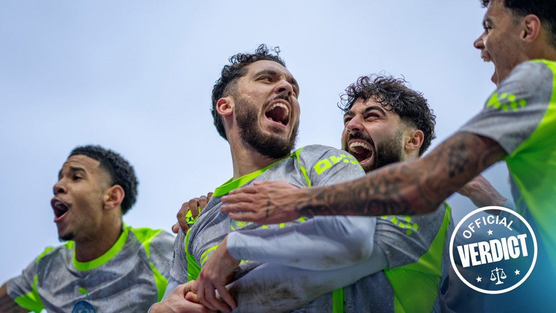 A group of soccer players huddling together, wearing gray and neon green jerseys. The image includes a sticker that says 'Official Verdict.'