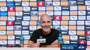 A man smiles during a press conference with Lucozade bottles on the table and various sponsor logos in the background.