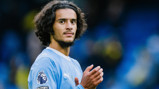 A Manchester City player wearing the team's kit, with the Premier League logo on the sleeve, clapping and facing the camera.