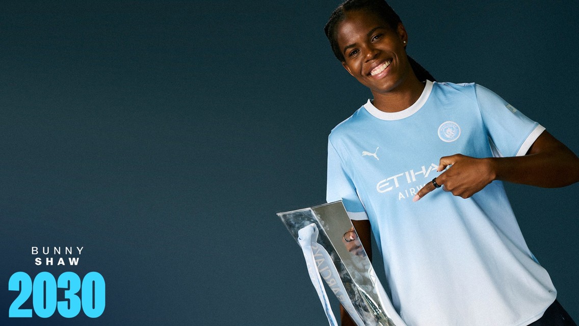 A person in a Manchester City football kit holding a shiny trophy with the text 'Bunny Shaw 2030'.