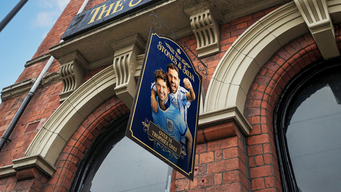 A pub sign titled 'Stones & Silva' featuring two footballers in Manchester City jerseys with the text 'Over 18 Trophies Only'.