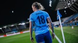 A soccer player wearing a Manchester City jersey with the number 18 approaches a corner flag on a field under stadium lights.